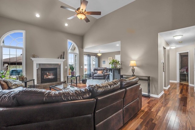 living room with high vaulted ceiling, ceiling fan, a fireplace, dark wood finished floors, and baseboards