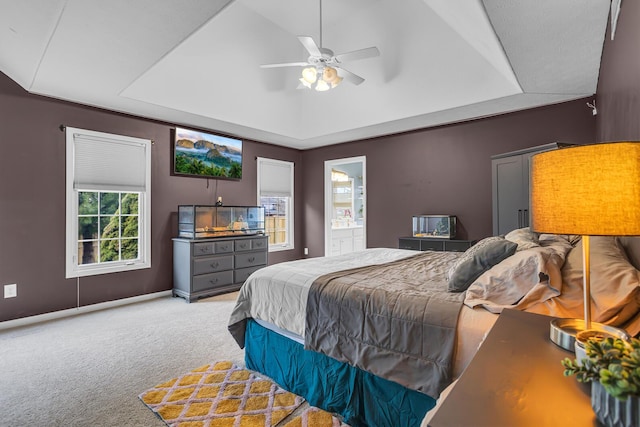 carpeted bedroom featuring baseboards, a ceiling fan, ensuite bathroom, and a raised ceiling