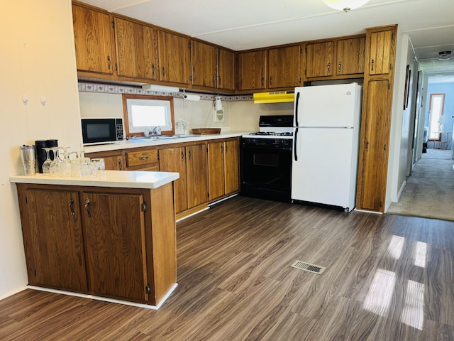 kitchen with visible vents, freestanding refrigerator, gas range, under cabinet range hood, and brown cabinets