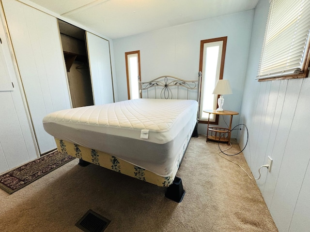 bedroom with light colored carpet, visible vents, and a closet