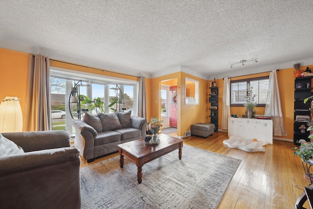 living area featuring wood-type flooring, plenty of natural light, a textured ceiling, and visible vents
