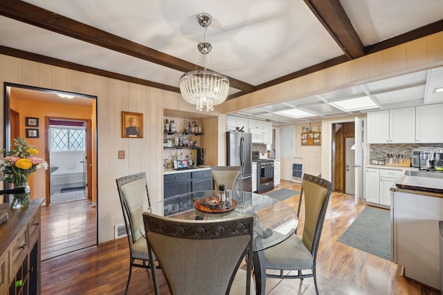 dining space with an inviting chandelier, visible vents, wood finished floors, and beamed ceiling