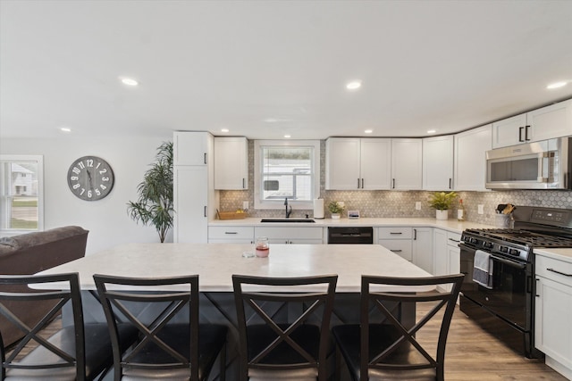 kitchen featuring black appliances, backsplash, a sink, and a breakfast bar