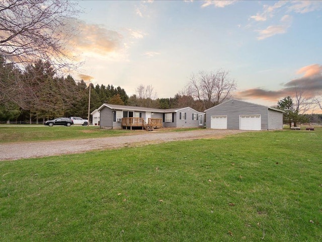 view of front of home featuring gravel driveway, a front lawn, a wooden deck, an outbuilding, and a detached garage