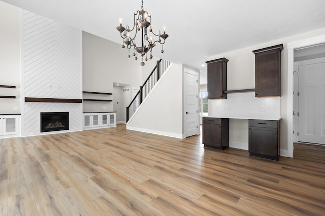 2630 Ashford Trl, Portage, MI 49024 - unfurnished living room with an inviting chandelier, stairway, a large fireplace, baseboards, and light wood-type flooring