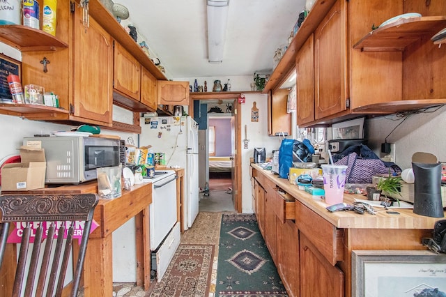 kitchen with stainless steel microwave, open shelves, brown cabinetry, light countertops, and electric stove