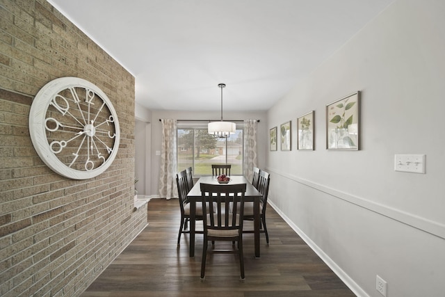 dining area featuring dark wood finished floors, brick wall, baseboards, and an inviting chandelier