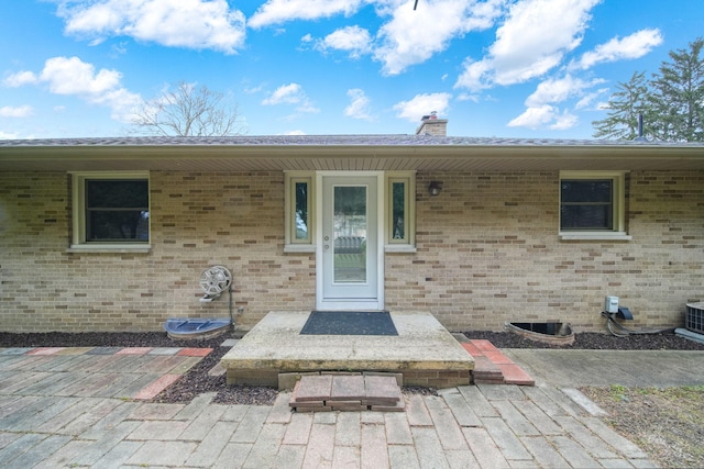 doorway to property with a chimney and brick siding