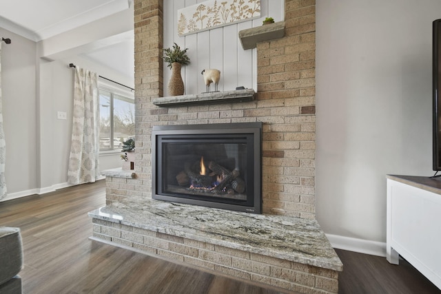 interior details featuring wood finished floors, a brick fireplace, baseboards, and crown molding