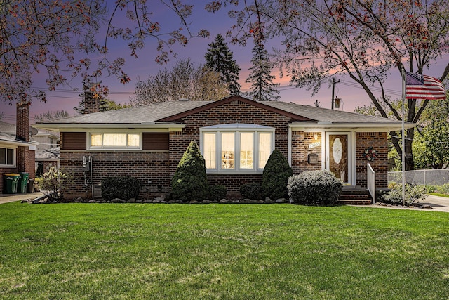 ranch-style home featuring a lawn, roof with shingles, and brick siding