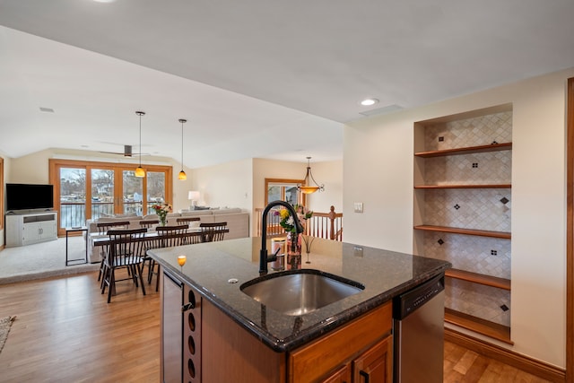 kitchen with stainless steel dishwasher, dark stone countertops, a sink, open floor plan, and light wood-style flooring