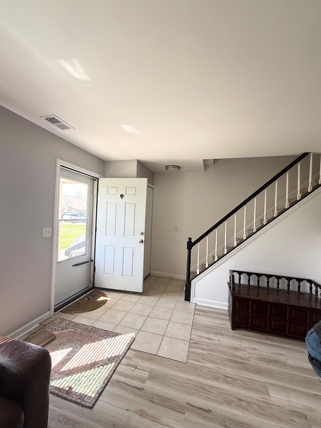foyer entrance with visible vents, stairs, baseboards, and light wood-type flooring