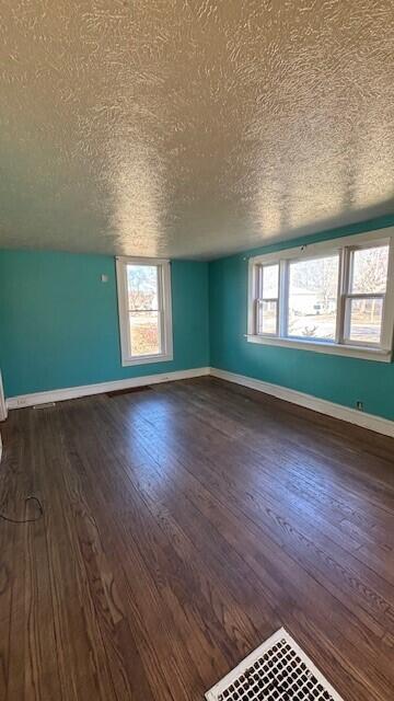 unfurnished room with dark wood finished floors, a textured ceiling, and a healthy amount of sunlight