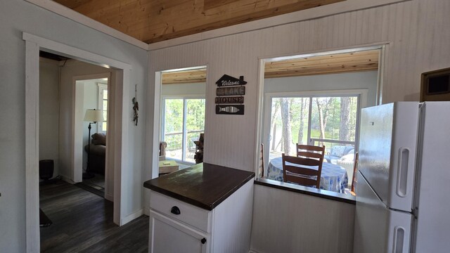 kitchen featuring white cabinets, wooden walls, wooden ceiling, freestanding refrigerator, and dark wood-style flooring