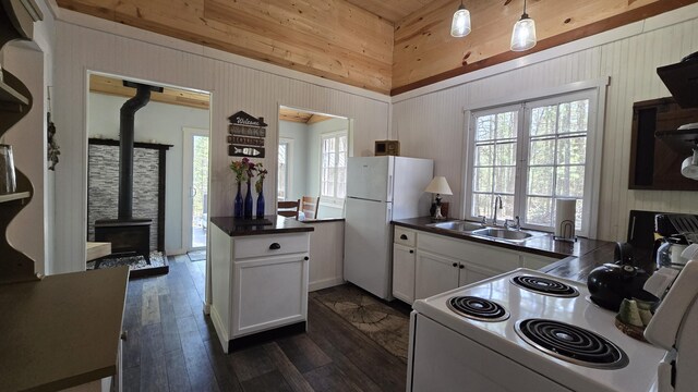 kitchen featuring dark countertops, a wood stove, a sink, and white appliances
