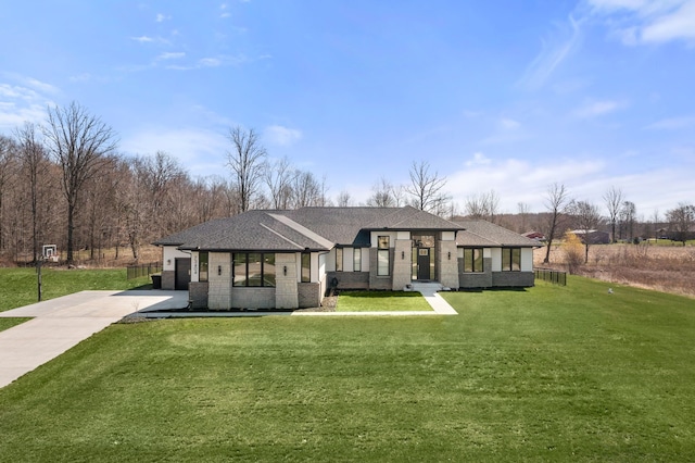 rear view of property featuring driveway, brick siding, a yard, and roof with shingles