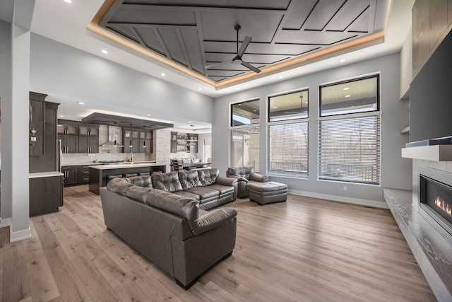 living area with baseboards, a glass covered fireplace, and a tray ceiling