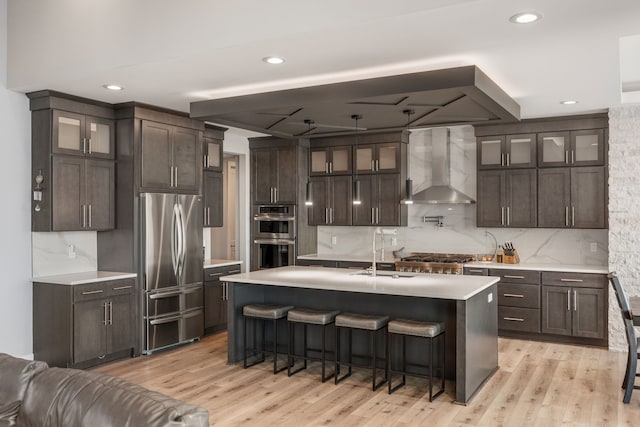kitchen with wall chimney range hood, dark brown cabinets, a sink, stainless steel appliances, and light countertops