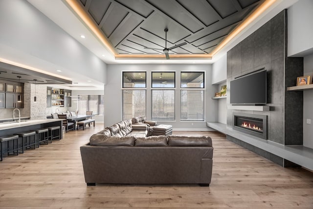 living area with light wood finished floors, a tiled fireplace, recessed lighting, and a raised ceiling