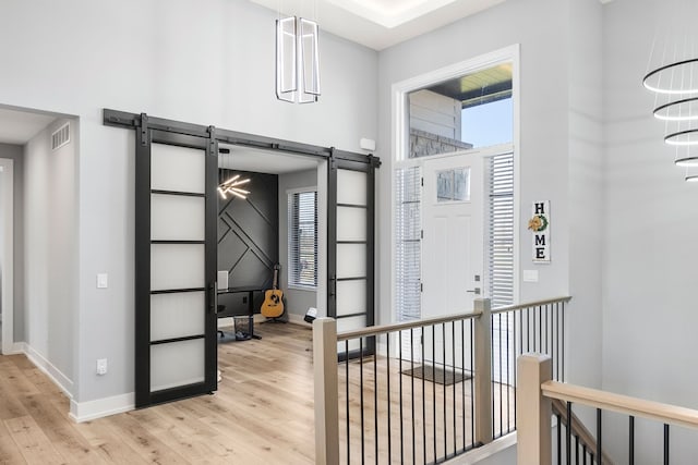 hallway with a barn door, light wood-style flooring, visible vents, and baseboards