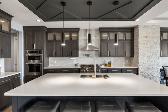 kitchen with tasteful backsplash, dark brown cabinets, a sink, double oven, and wall chimney exhaust hood