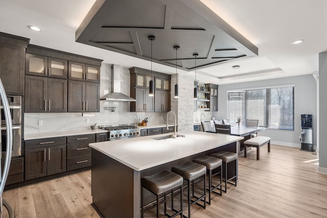 kitchen with wall chimney exhaust hood, light wood finished floors, a sink, baseboards, and decorative backsplash