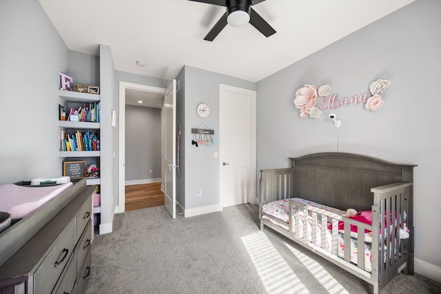 carpeted bedroom featuring a crib, baseboards, and ceiling fan