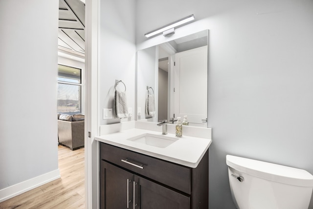 half bathroom with baseboards, wood finished floors, vanity, and toilet