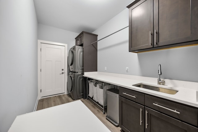 kitchen with light wood finished floors, stacked washer and dryer, a sink, dark brown cabinetry, and light countertops