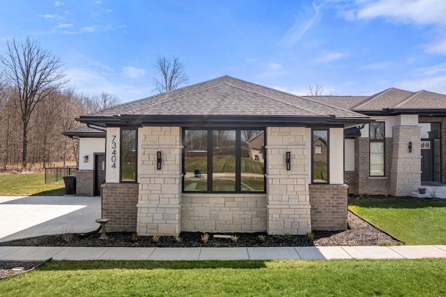 view of front of house with stone siding, a front lawn, and roof with shingles