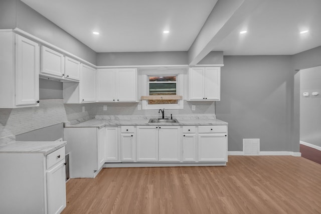 kitchen featuring a sink, tasteful backsplash, light wood-type flooring, visible vents, and white cabinetry