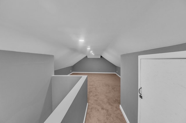 interior space with light carpet, vaulted ceiling, and baseboards