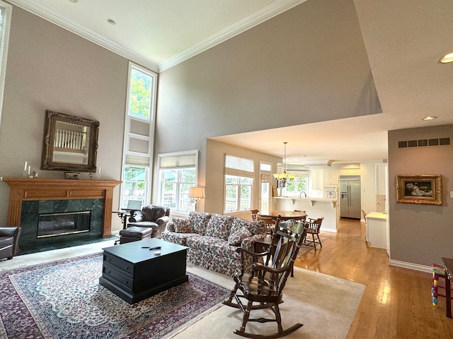 living area featuring crown molding, light wood-type flooring, a premium fireplace, baseboards, and visible vents