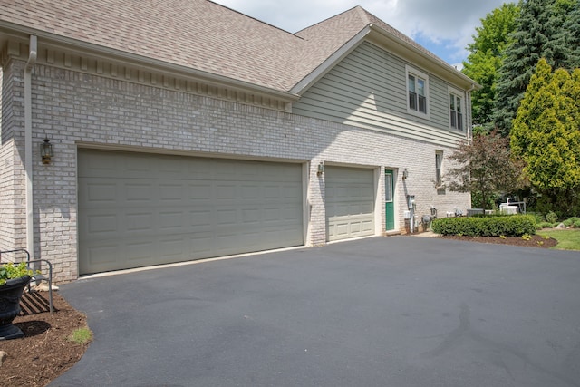 view of home's exterior with brick siding, driveway, a shingled roof, and a garage