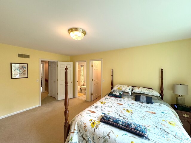 bedroom featuring ensuite bath, baseboards, visible vents, and light colored carpet
