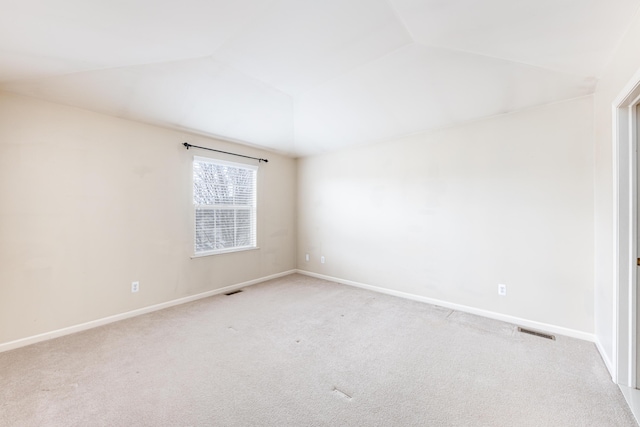 spare room featuring light carpet, vaulted ceiling, visible vents, and baseboards