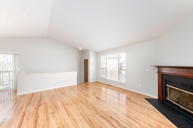 unfurnished living room with a fireplace with flush hearth, lofted ceiling, wood finished floors, and baseboards