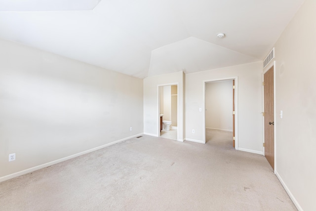 unfurnished bedroom with vaulted ceiling, baseboards, visible vents, light colored carpet, and ensuite bath