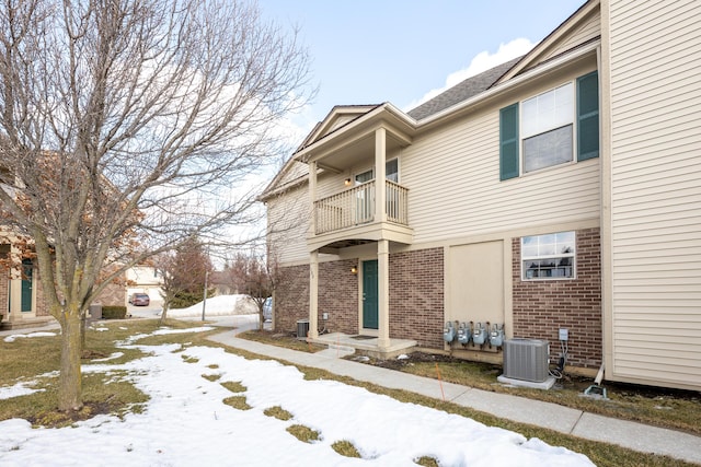 exterior space with central AC unit, brick siding, and a balcony