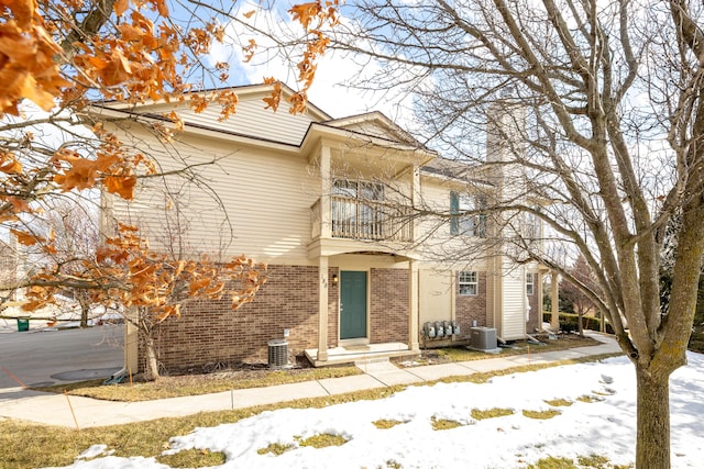 traditional home featuring central air condition unit, brick siding, and a balcony