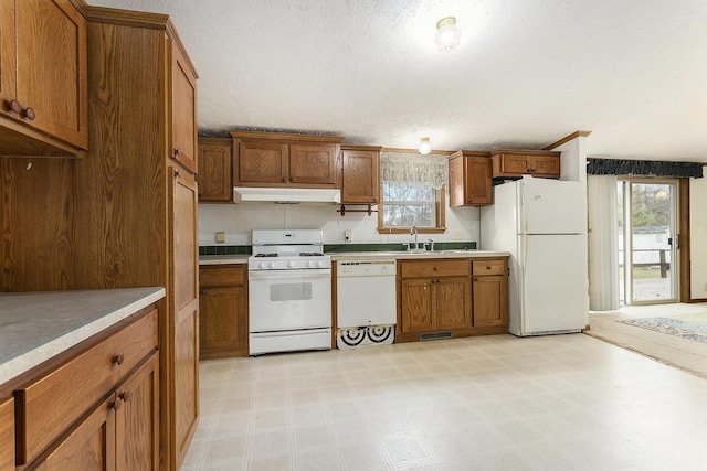 kitchen featuring brown cabinetry, a wealth of natural light, under cabinet range hood, and white appliances