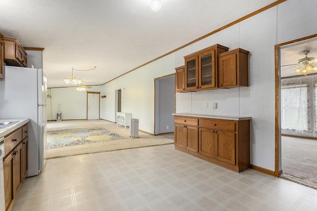 kitchen featuring brown cabinets, an inviting chandelier, light countertops, ornamental molding, and glass insert cabinets