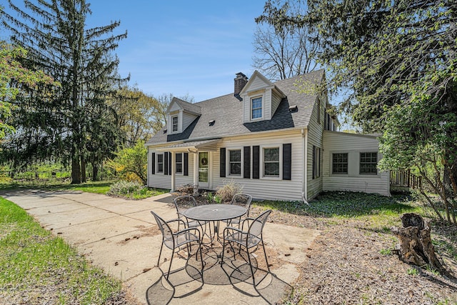rear view of house with a chimney, a shingled roof, and a patio area