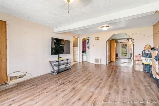 unfurnished living room with wood finished floors, visible vents, arched walkways, beam ceiling, and a textured ceiling