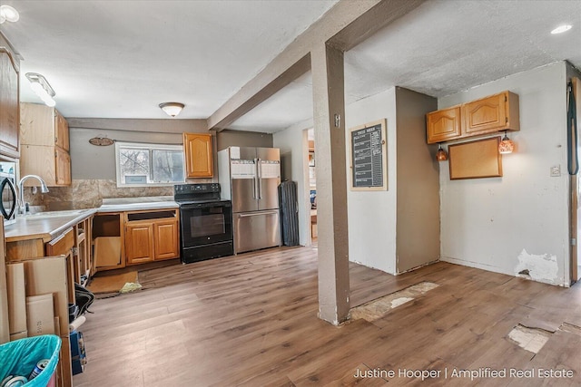 kitchen with black range with electric stovetop, a sink, freestanding refrigerator, light wood-style floors, and tasteful backsplash