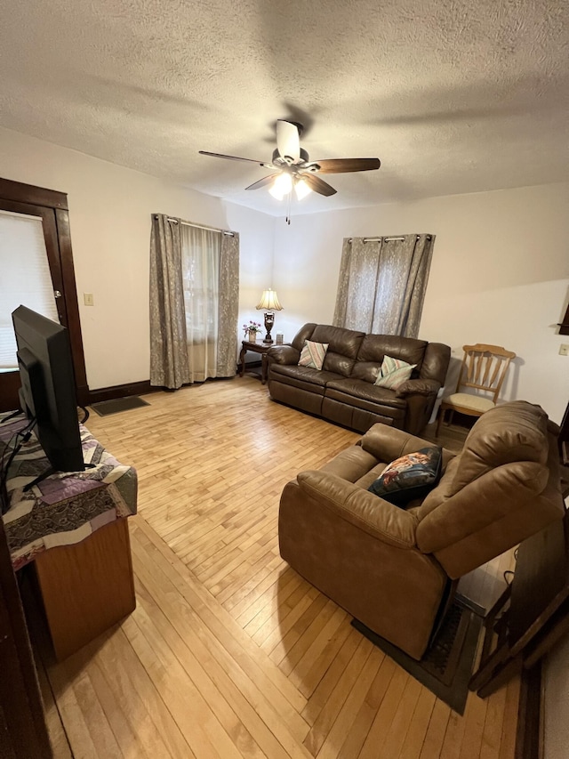 living room with light wood-style flooring, a textured ceiling, a ceiling fan, and baseboards