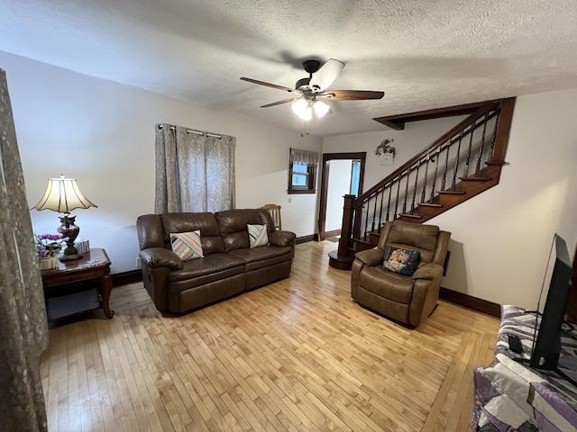 living room with a textured ceiling, light wood-type flooring, baseboards, a ceiling fan, and stairs