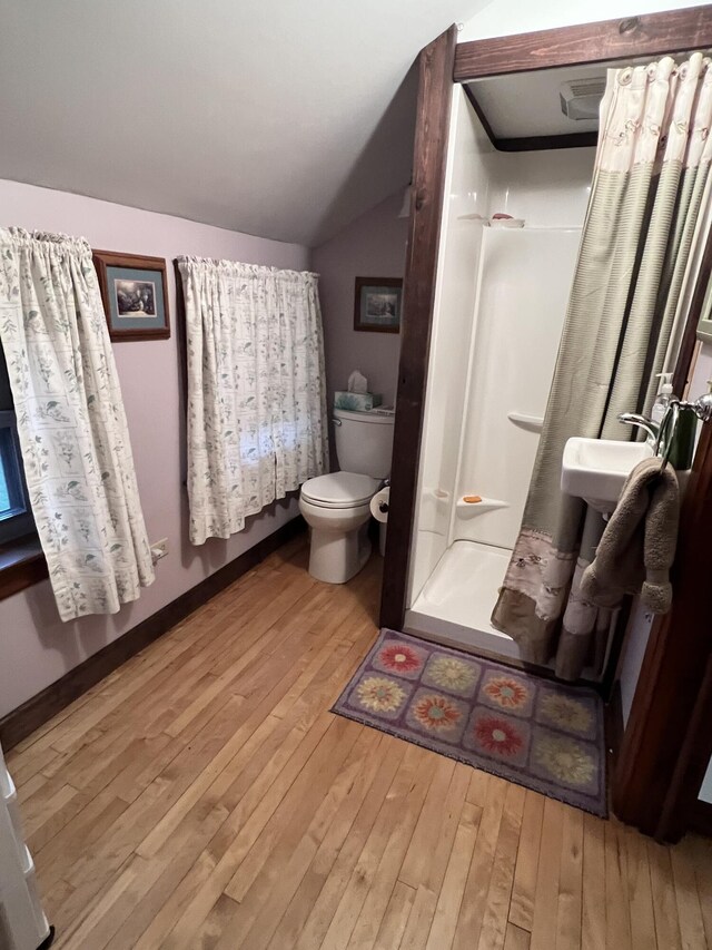 bathroom featuring wood-type flooring, vaulted ceiling, a shower stall, and toilet