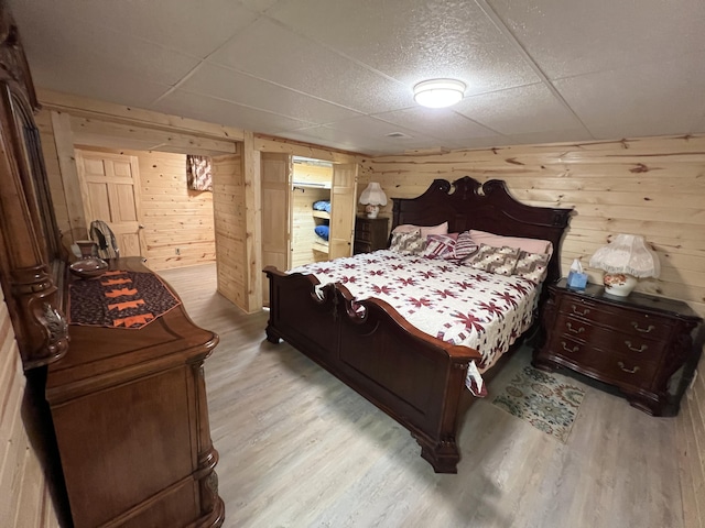 bedroom with wood walls, light wood finished floors, and a paneled ceiling