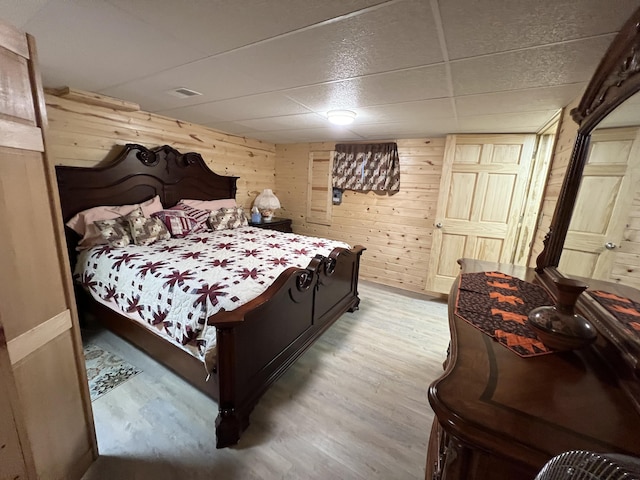 bedroom featuring a paneled ceiling, light wood-style flooring, and wooden walls
